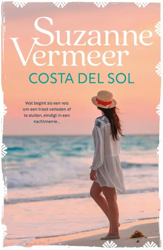 Een vrouw in een geborduurde witte jurk en strooien hoed met rode band staat op het strand bij costa del sol