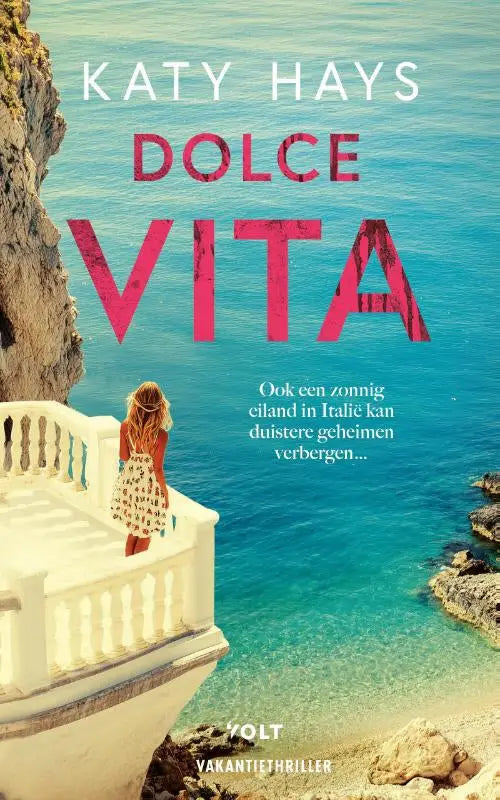 A woman in a white dress with black floral patterns stands on a sunlit balcony overlooking turquoise waters dolce vita katy hays spannende boeken algemeen