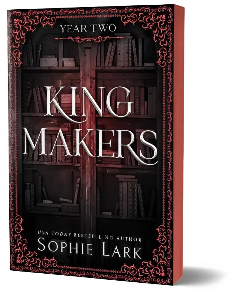 Rood hardcover boek king makers van sophie lark met donkere houten boekenplank en roze sierlijke rand in spicy forbidden dark college romance kingmakers year two