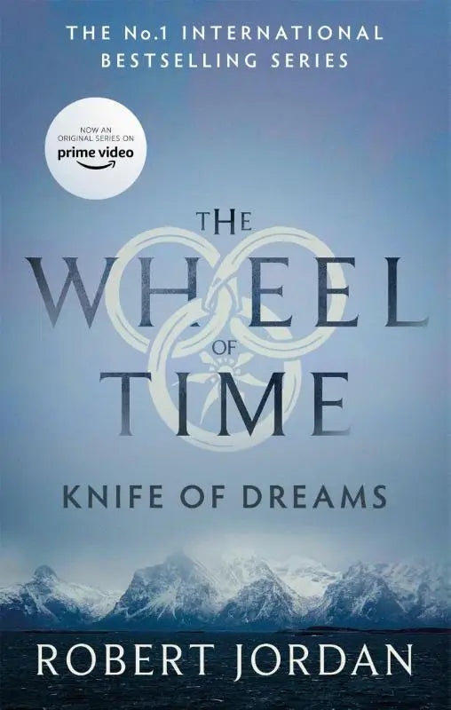 De knife of dreams boek 11 van the wheel met een zilveren wielembleem en besneeuwde bergen nu een major tv serie