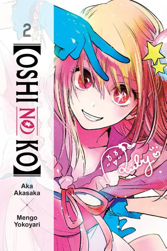 De cover van het tweede volume van oshi no ko manga toont jonge vrouw met roze en blonde haren en roodogige in roze outfit met steraccessoires