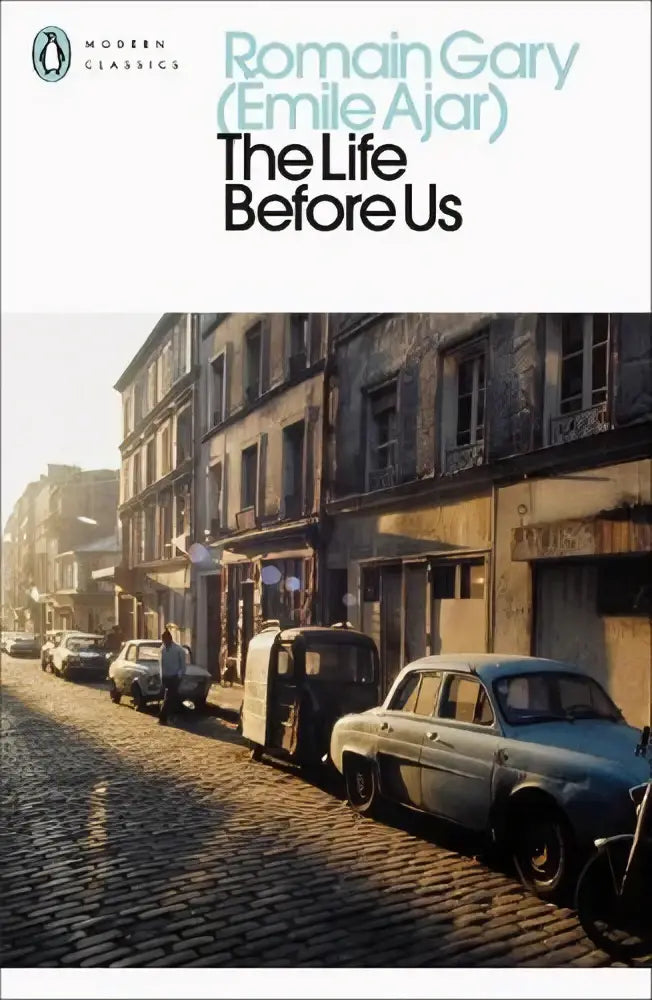 A paperback copy of the life before us by romain gary with a muted sepia cover showing a sunlit european street scene