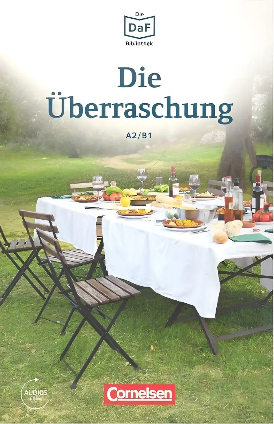 De cover van de die überraschung a2 b1 audiobook van cornelsen toont een wit tafelkleed op een buiten eettafel met eten en drinken onder mistige bomen voor daf daz-lerenden