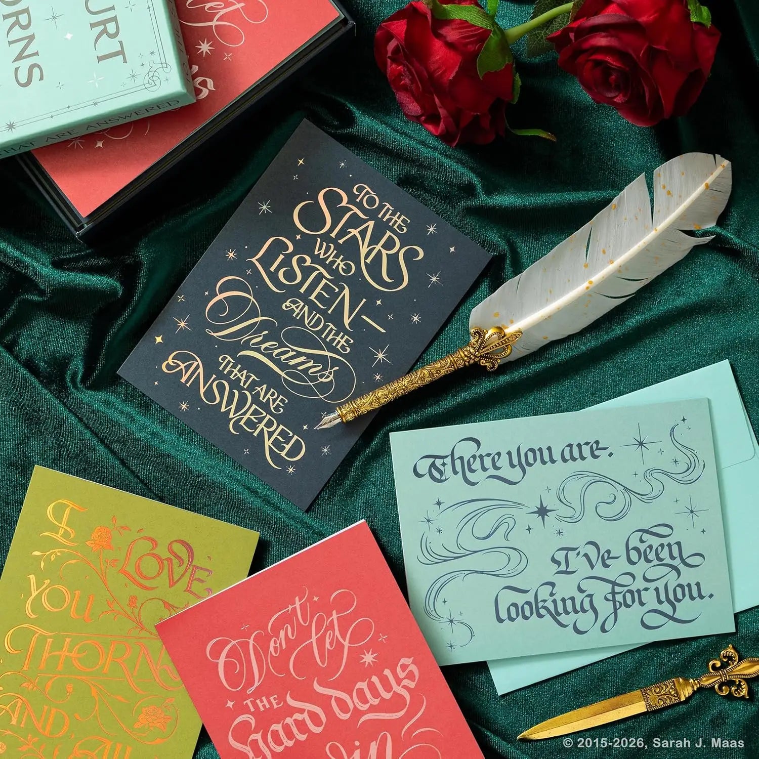 Een goudkleurige veerpen met een sierlijk verguld handvat ligt op een donkerblauwe notecard met thorns and roses official gilded sterrenmotief
