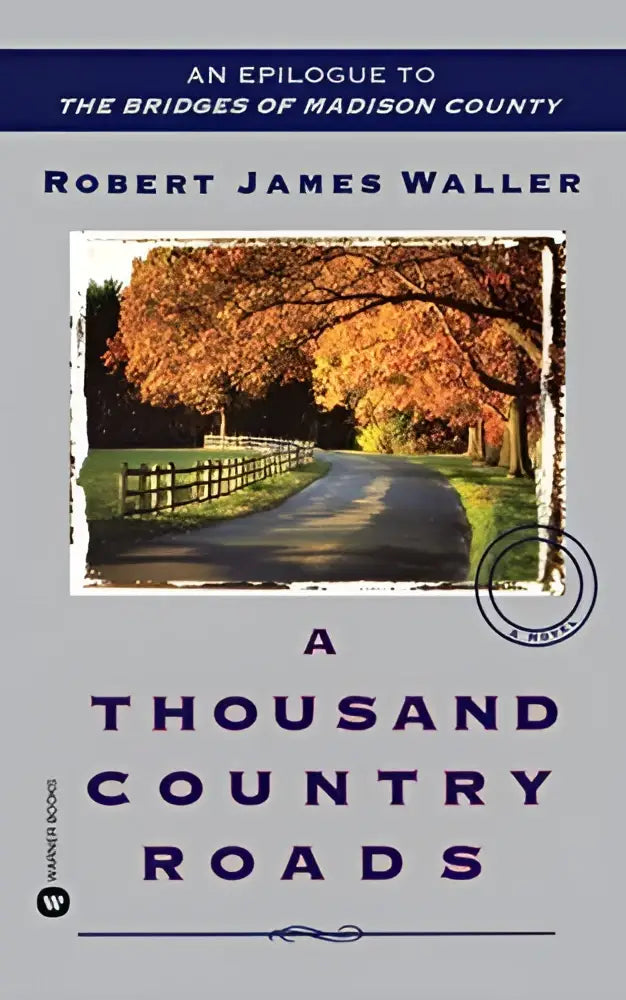 Een grijs boek met een foto van een herfstweg met oranje bomen en houten hek, getiteld a thousand country roads door robert james waller
