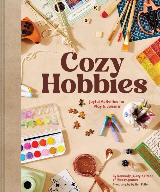 Cozy hobbies joyful book cover with beige background and scattered craft supplies like paintbrushes and puzzle pieces