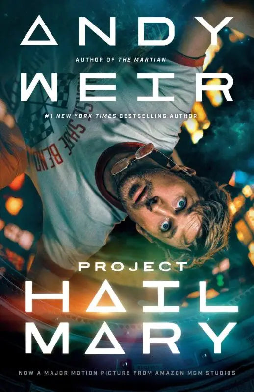 De book cover van project hail mary movie tie-in toont een man in een wit t-shirt met rode letters tegen een verlichte stadsachtergrond