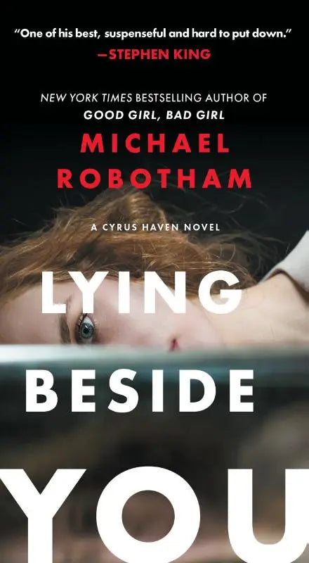 De boekcover van lying beside you door michael robotham toont een vrouw met lichtbruin haar en blauwe ogen, deels bedekt door een donkere balk