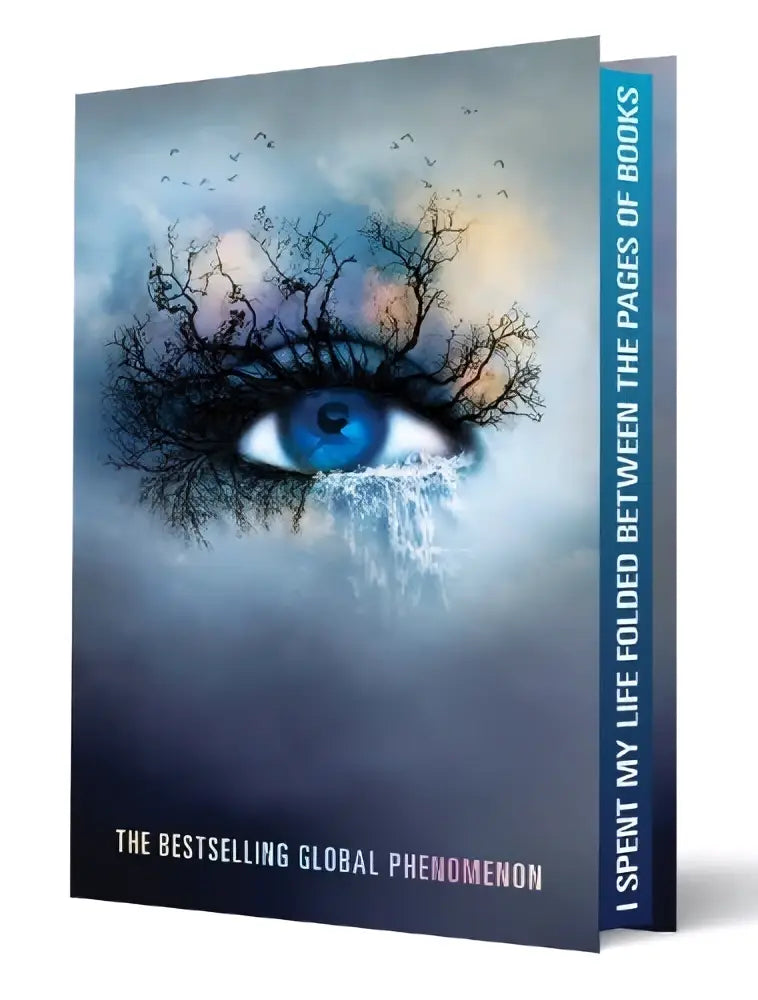 A hardcover deluxe limited edition book shatter me featuring a vivid blue eye and dark tree-like branches on the cover