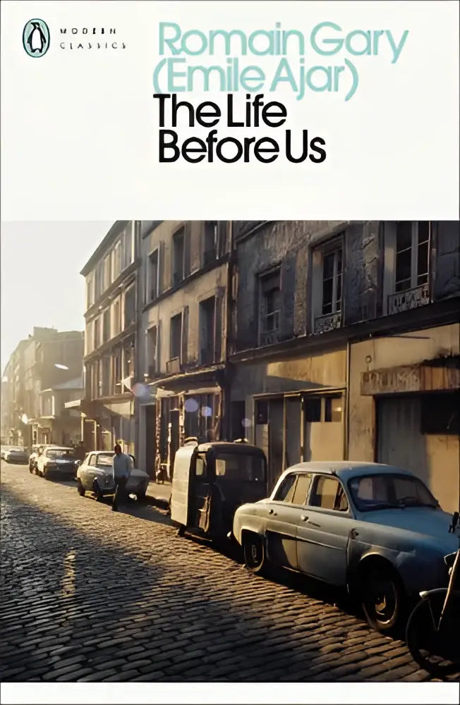 A paperback edition of the life before us by romain gary with a muted sepia cover showing a sunlit european street scene