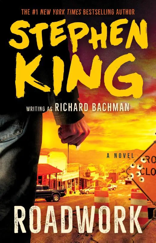 Gele en zwarte boekomslag van the roadwork door stephen king met een hand die een gereedschap vasthoudt bij een oranje wegwerk scène