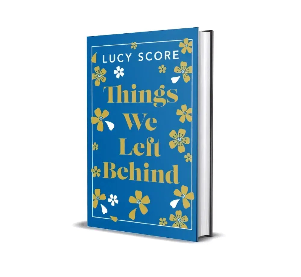 Blauw hardback boek met gouden bloemenpatroon en witte bloemen getiteld things we left behind van lucy score
