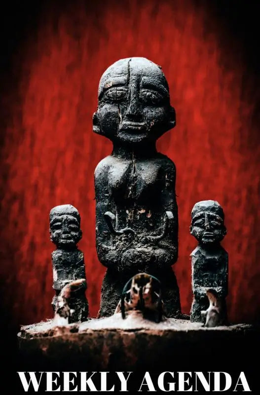 Donkere verweerde stenen beeldhouwwerk met centraal figuur en twee kleinere figuren op sokkel vodun agenda